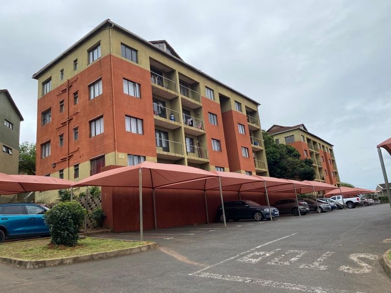 Exterior view of a multi-story apartment complex featuring covered parking bays and balconies.