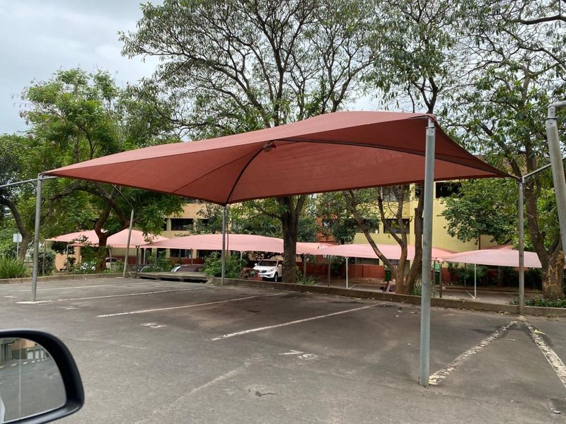 Outdoor parking area featuring covered shade net structures for vehicle protection within the apartment complex grounds.