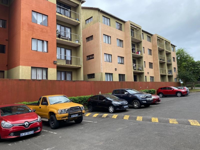 Exterior view of a multi-story apartment complex featuring private balconies and a paved parking area for residents.