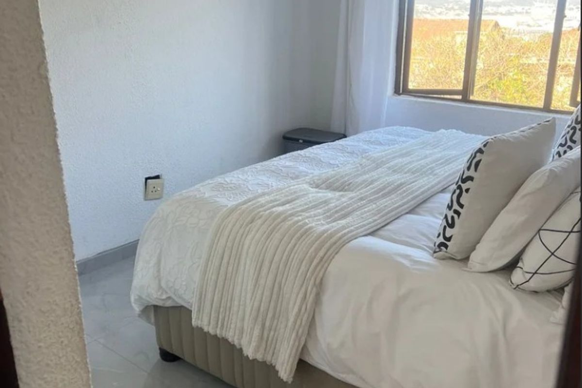 A bright bedroom featuring tiled flooring, a large window with natural light, and neutral wall finishes.