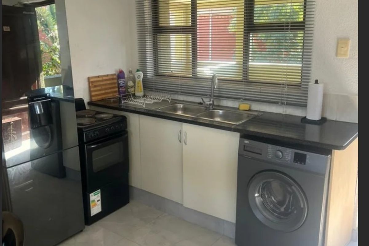 Compact kitchen featuring tiled flooring, laminate countertops, a double sink, and space for a freestanding stove and washing machine.