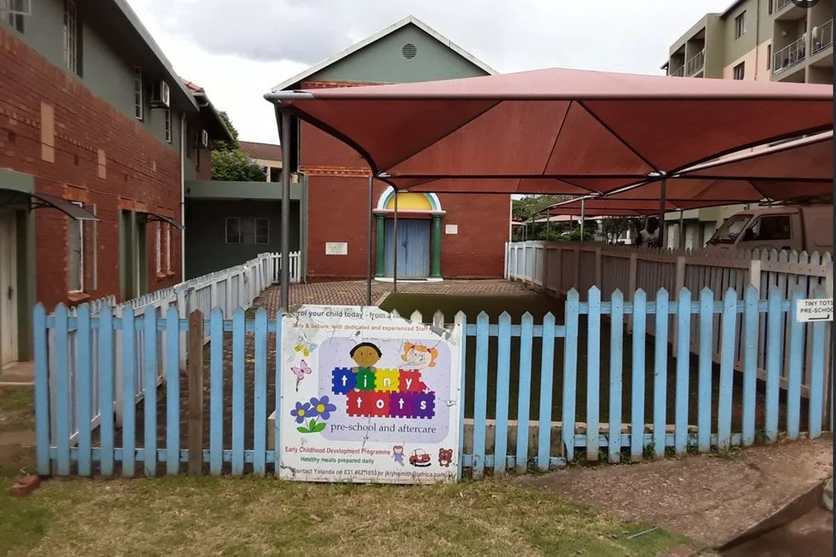 Exterior view of a courtyard area featuring a shaded play space, perimeter fencing, and brick building facades.