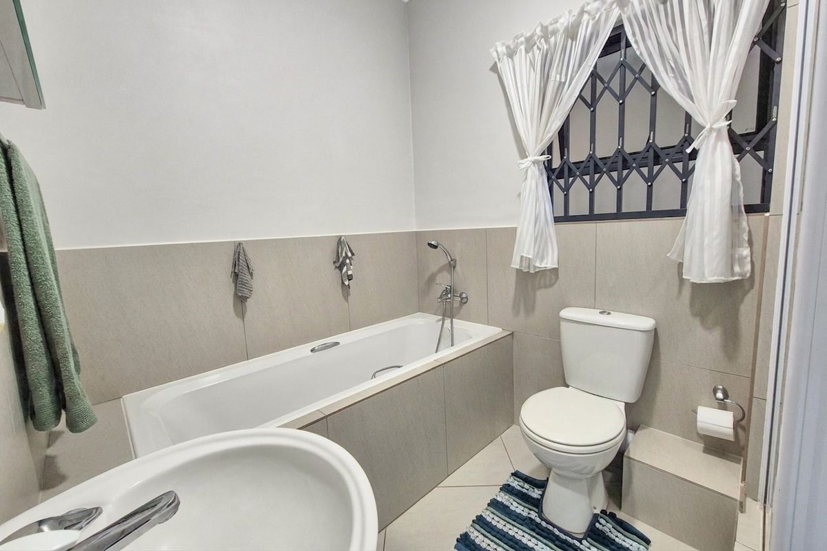 A functional bathroom featuring a built-in bathtub, a standard toilet, and tiled wall finishes with a security gate on the window.