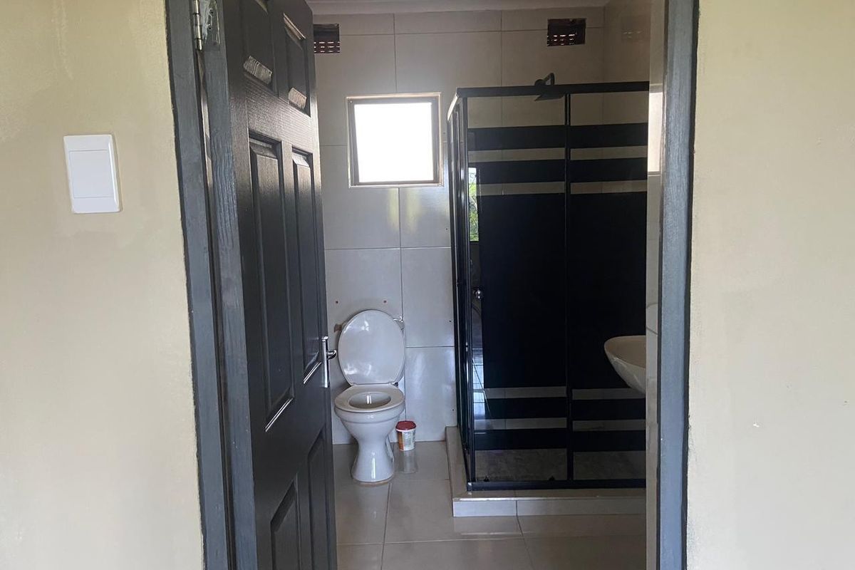 A functional bathroom featuring a glass-enclosed shower, ceramic toilet, and wall-mounted basin with neutral tiled walls and flooring.
