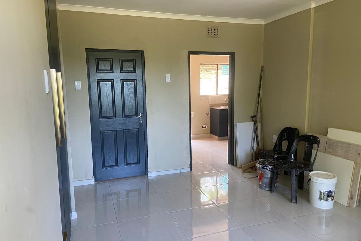 Interior view of a living area featuring tiled flooring, a dark panelled door, and an open doorway leading to an adjacent kitchen space.