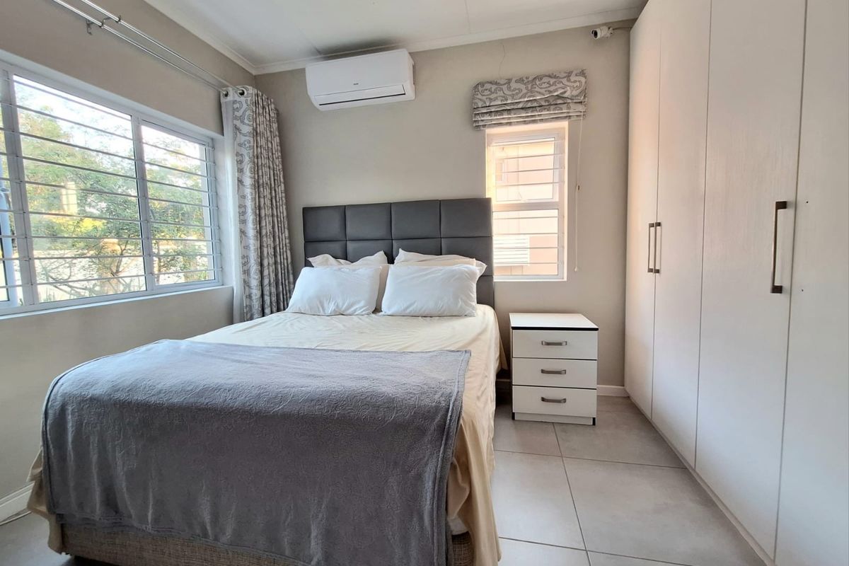 A well-maintained bedroom featuring large format floor tiles, built-in cupboards, a wall-mounted air conditioning unit, and security bars on the windows.