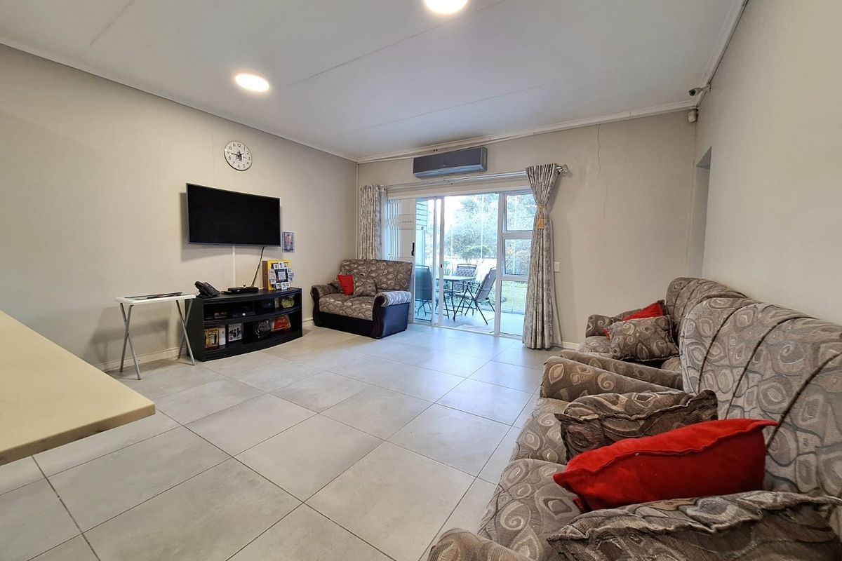 Spacious living room featuring large floor tiles, recessed ceiling lighting, wall-mounted air conditioning unit, and sliding glass doors leading to an outdoor patio area.