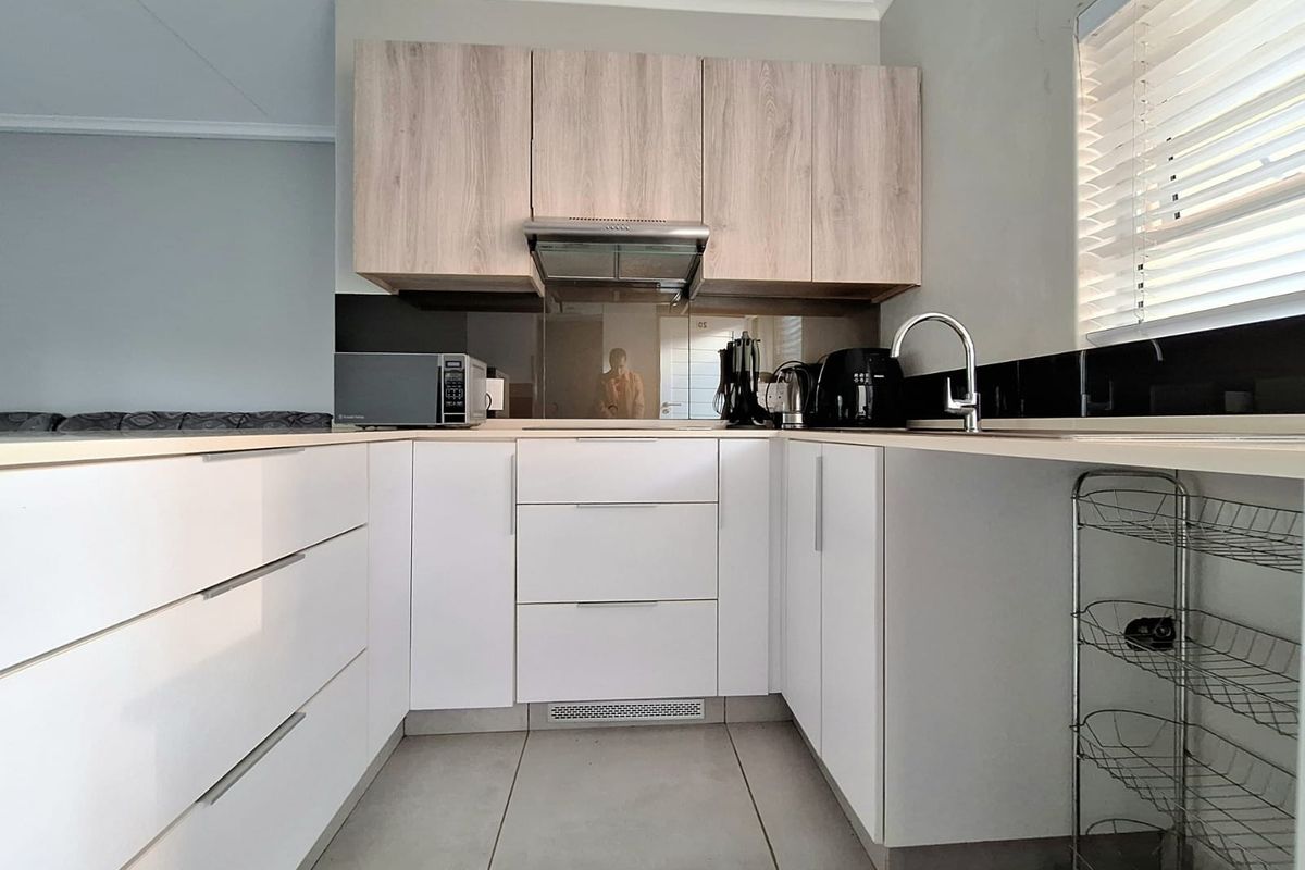 Modern U-shaped kitchen featuring white cabinetry, light wood-tone upper cupboards, a stainless steel extractor fan, and a sleek black glass splashback.