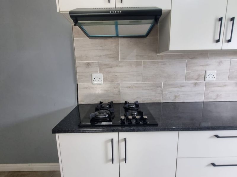Modern kitchen area featuring white cabinetry, dark granite countertops, a gas hob, and a sleek extractor fan with a neutral tiled backsplash.