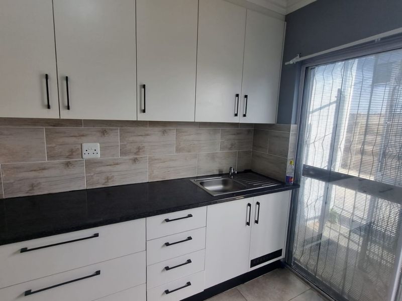 A clean, modern kitchen featuring white cabinetry, dark stone countertops, wood-look tiled backsplash, and direct access to an outdoor area via a sliding glass door.