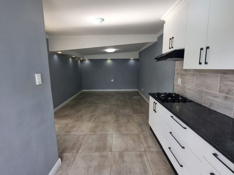 Spacious open-plan living area featuring a modern kitchen with white cabinetry, dark countertops, gas hob, and neutral tiled flooring throughout.