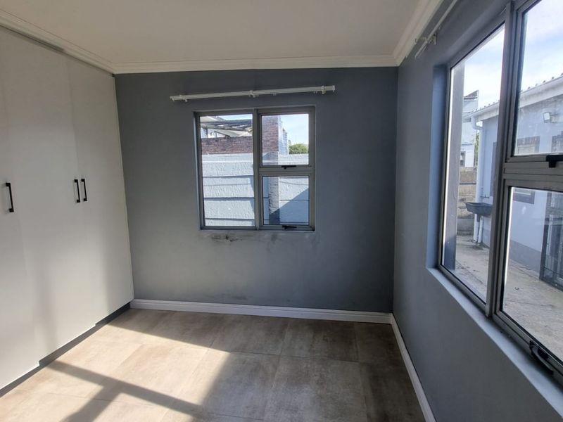 A bright, empty bedroom featuring tiled flooring, built-in cupboards, and aluminium window frames, offering a clean canvas for personalization.