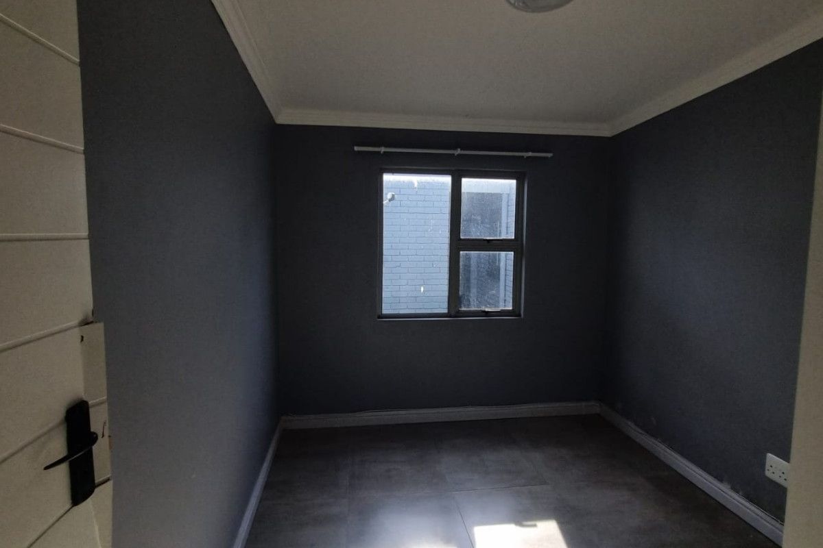 An empty bedroom featuring dark grey walls, tiled flooring, and a central ceiling light, offering a blank canvas for personalization.