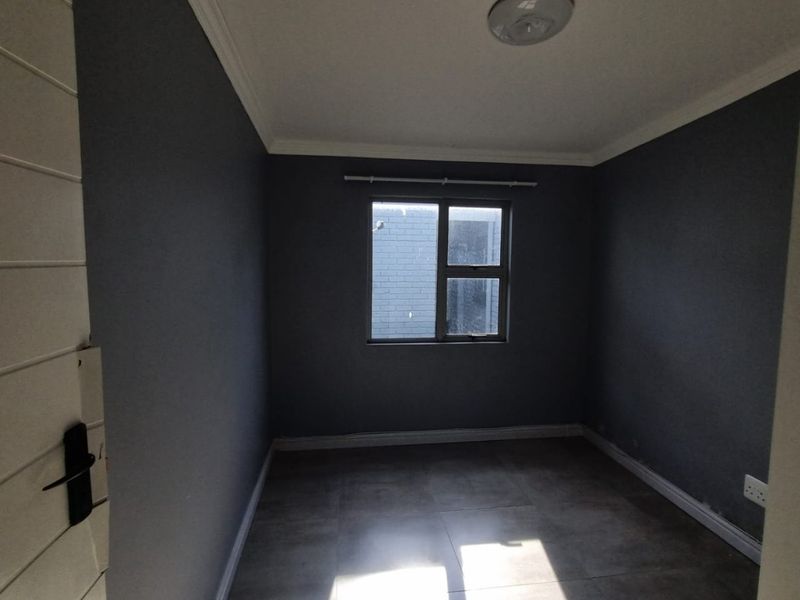 An empty bedroom featuring dark grey walls, tiled flooring, and a central ceiling light, offering a blank canvas for personalization.