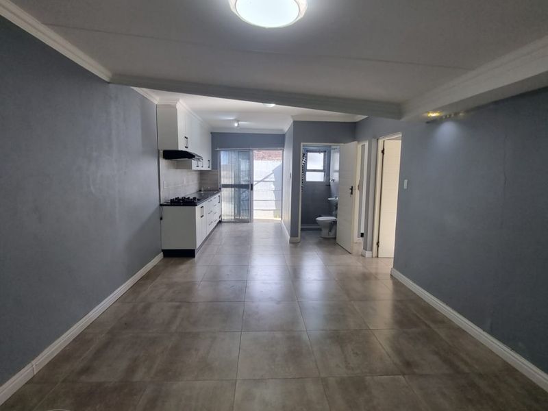 An open-plan living and kitchen area featuring neutral tiled flooring, modern cabinetry with a built-in hob, and access to an outdoor space.