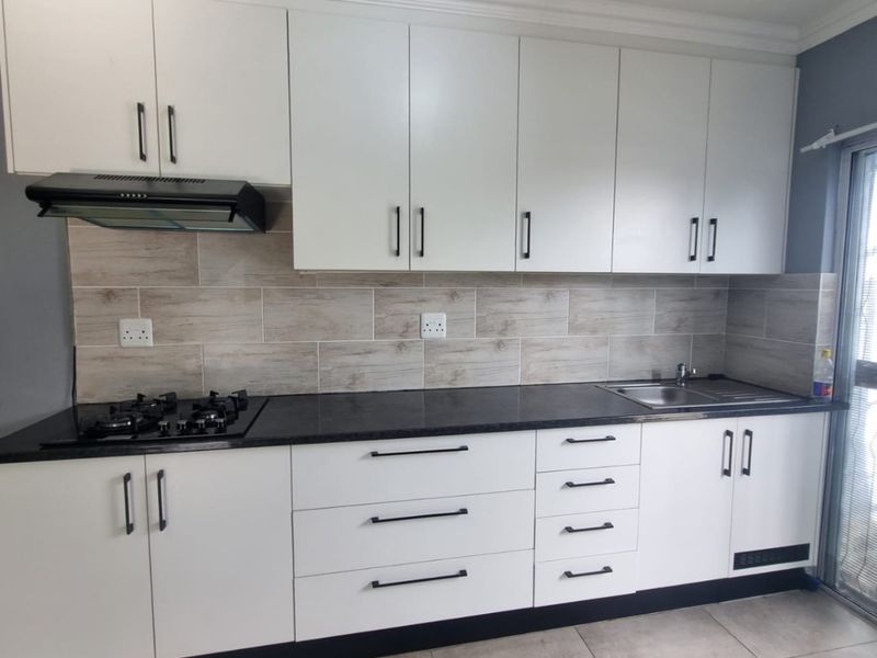 Modern kitchen featuring white cabinetry, dark stone countertops, a gas hob with extractor fan, and a tiled backsplash.