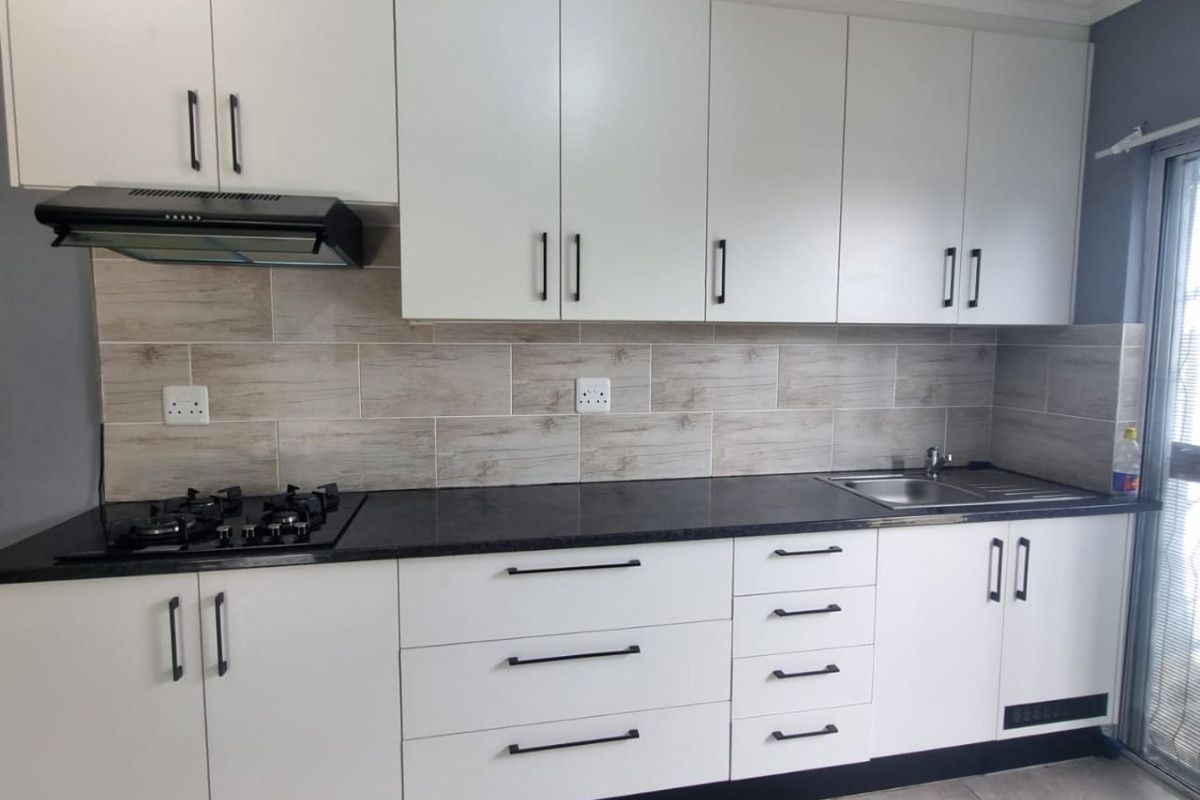 Modern kitchen featuring white cabinetry, dark stone countertops, a gas hob with extractor fan, and a tiled backsplash.