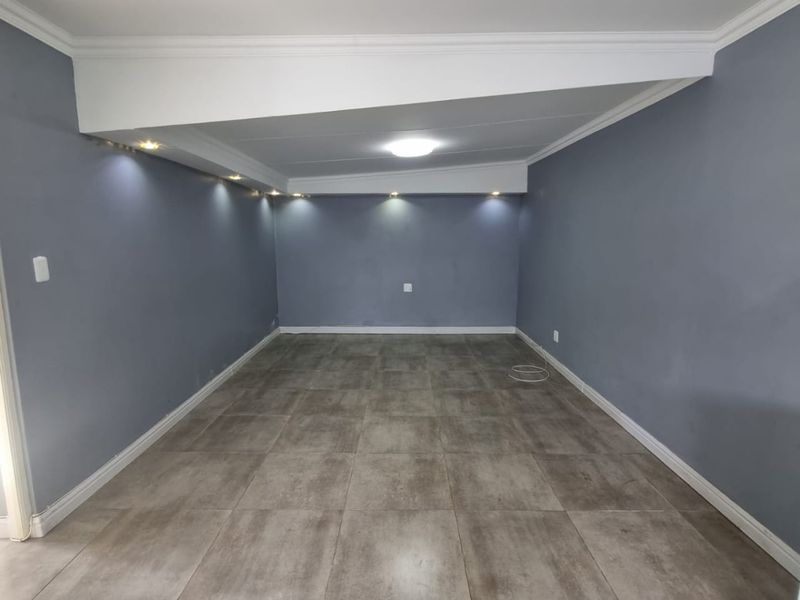 A spacious, empty living area featuring modern grey tiled flooring, recessed downlighting, and decorative cove molding, providing a clean and versatile blank canvas.