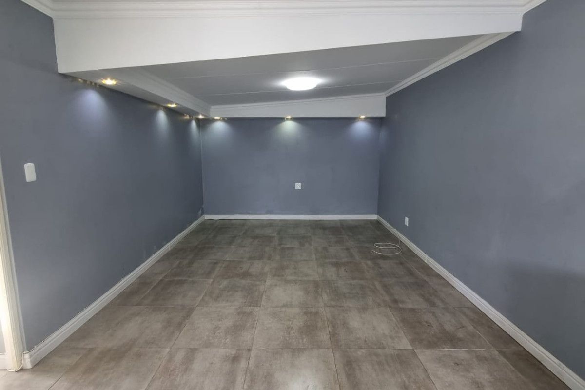 A spacious, empty living area featuring modern grey tiled flooring, recessed downlighting, and decorative cove molding, providing a clean and versatile blank canvas.