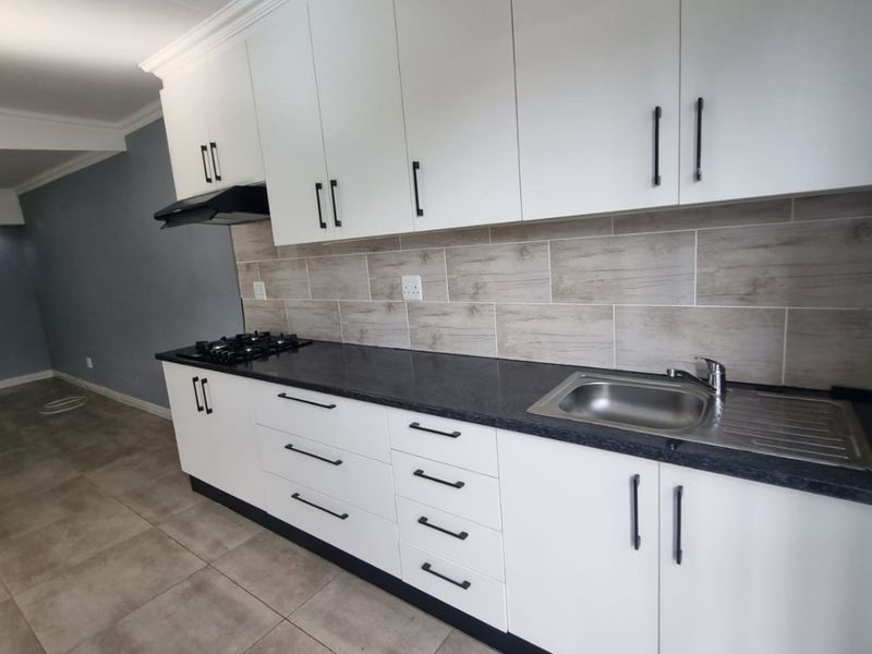 Modern kitchen featuring white cabinetry, dark granite countertops, a gas hob with extractor fan, and neutral tiled backsplash and flooring.