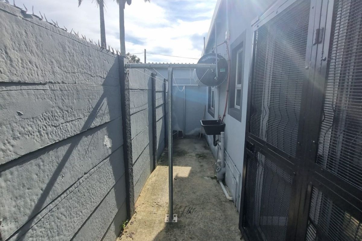 A narrow rear utility area featuring a concrete boundary wall with security spikes, a fitted utility sink, and a metal washing line.