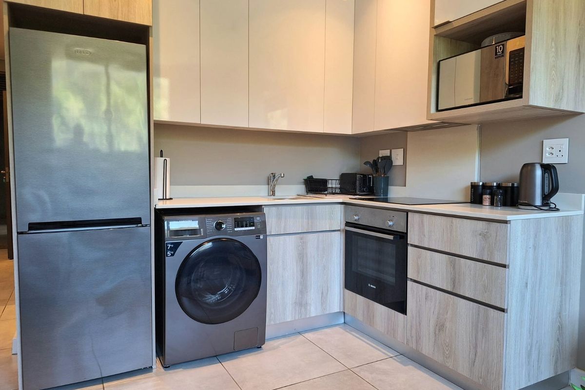 Modern kitchen featuring sleek cabinetry, integrated oven, hob, and built-in laundry appliance space with tiled flooring.