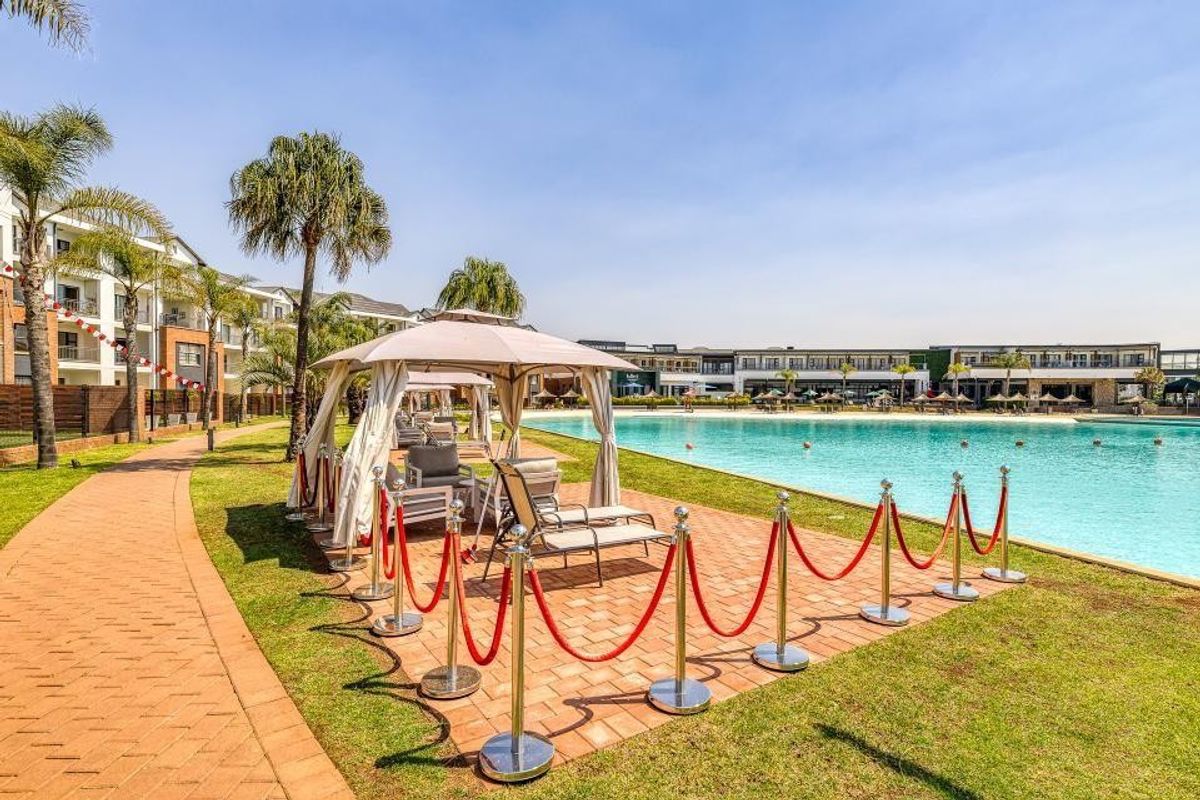 A well-maintained communal pool area featuring a large swimming pool, paved walkways, and landscaped gardens within an apartment complex.