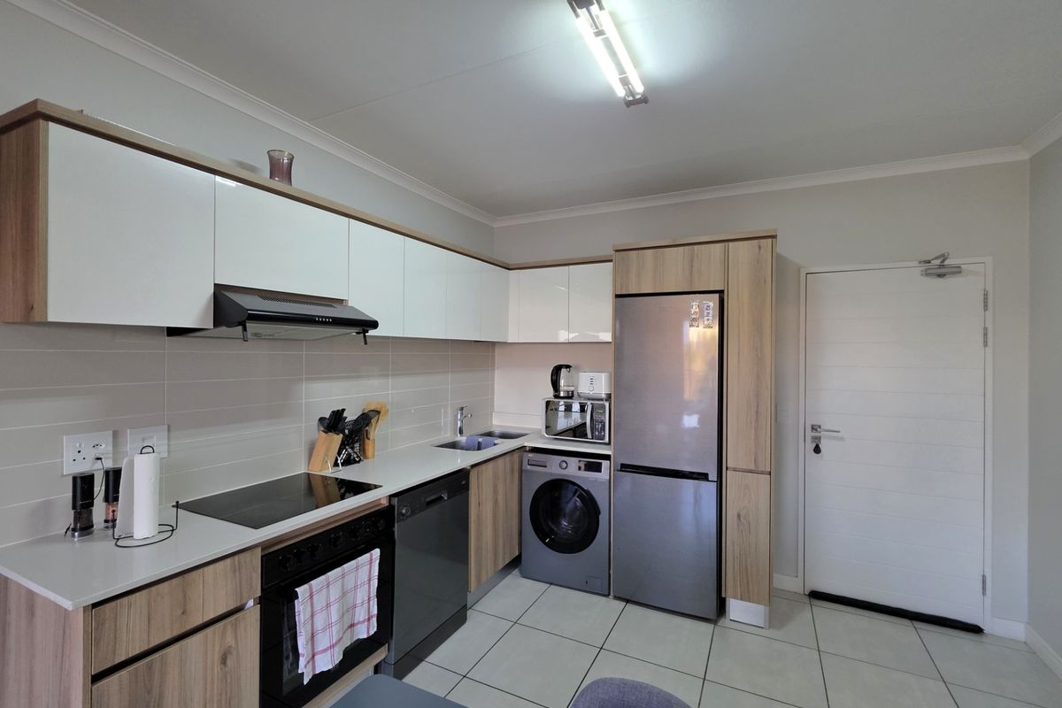 Modern kitchen featuring sleek white and wood-grain cabinetry, integrated appliances, a built-in hob, extractor fan, and tiled flooring.