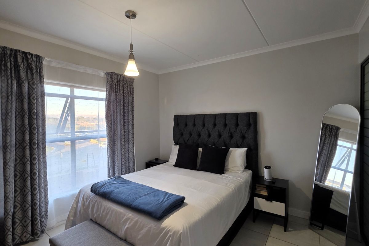A well-lit bedroom featuring tiled flooring, a large window with curtains, and a central pendant light fixture.