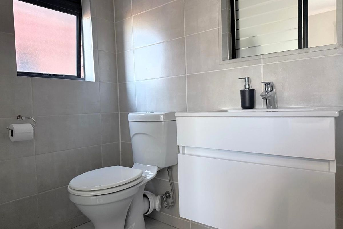Modern bathroom featuring neutral wall tiles, a wall-mounted vanity with integrated basin, and a standard toilet.