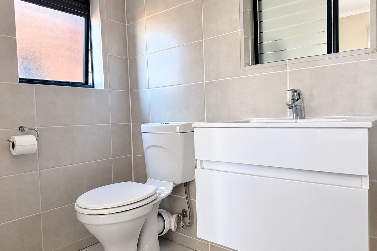 A modern, well-maintained bathroom featuring a wall-mounted vanity with a basin, a toilet, and neutral wall and floor tiling.