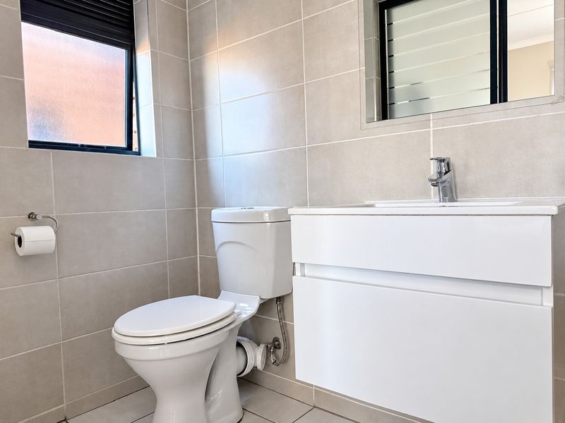 A modern, well-maintained bathroom featuring a wall-mounted vanity with a basin, a toilet, and neutral wall and floor tiling.