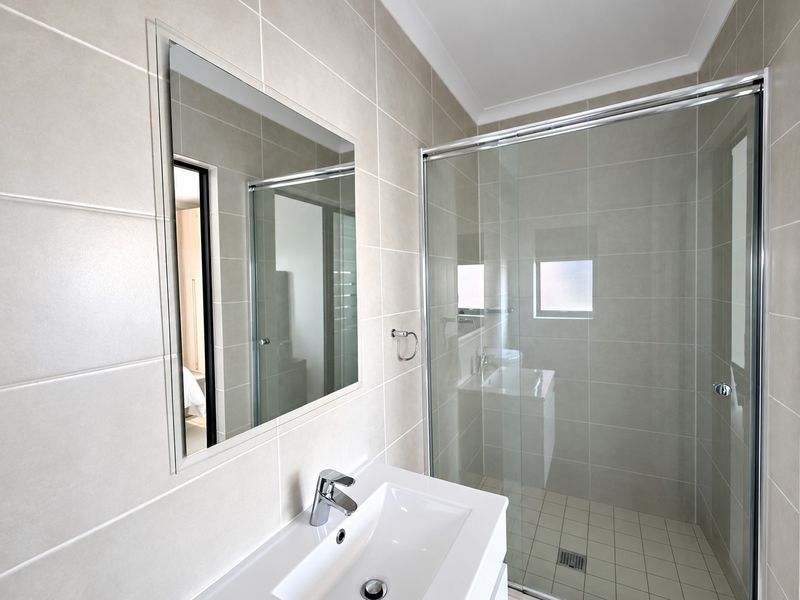 A clean, modern bathroom featuring a glass-enclosed shower, wall-mounted mirror, and a sleek vanity basin with chrome fixtures.