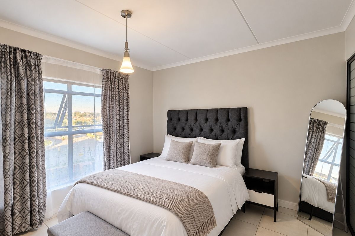 A well-maintained bedroom featuring neutral wall tones, tiled flooring, and a large window that provides ample natural light.