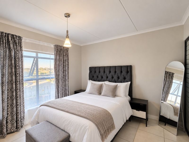 A well-maintained bedroom featuring neutral wall tones, tiled flooring, and a large window that provides ample natural light.