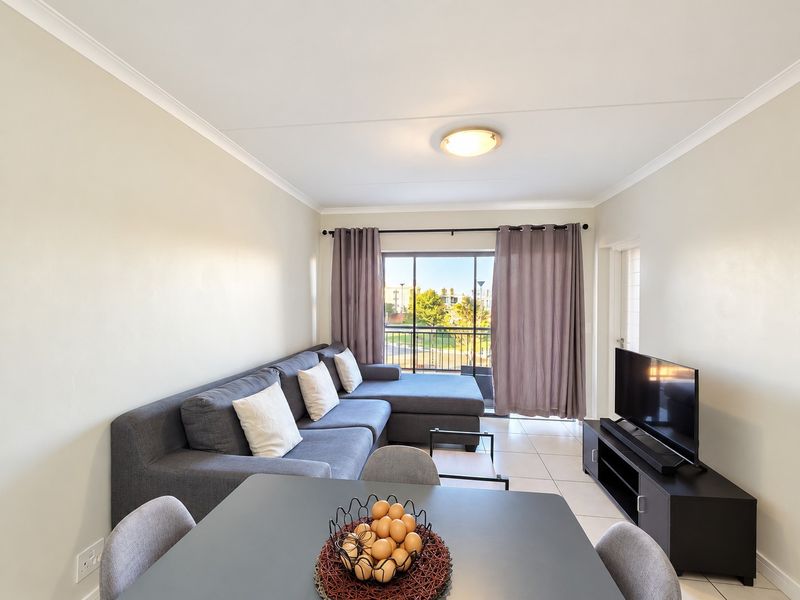 An open-plan living area featuring tiled flooring, neutral walls, and a sliding glass door providing access to an outdoor balcony.