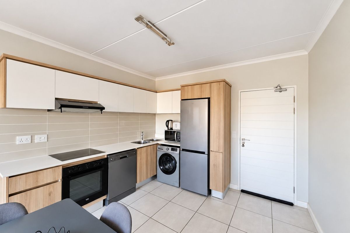 Modern kitchen featuring light wood and white cabinetry, integrated appliances, electric hob, oven, and tiled flooring with a clean, functional layout.