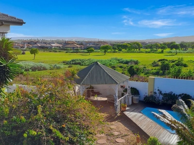 Elevated view of the rear garden featuring a swimming pool, wooden decking, and a gazebo, overlooking a scenic green landscape.
