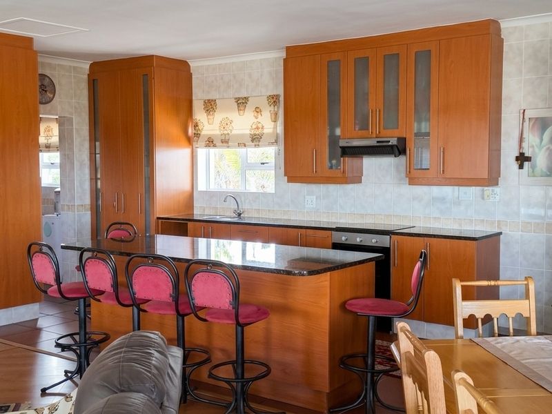 Open-plan kitchen featuring wood-finish cabinetry, granite countertops, and a central island, seamlessly integrated with the dining and living areas.