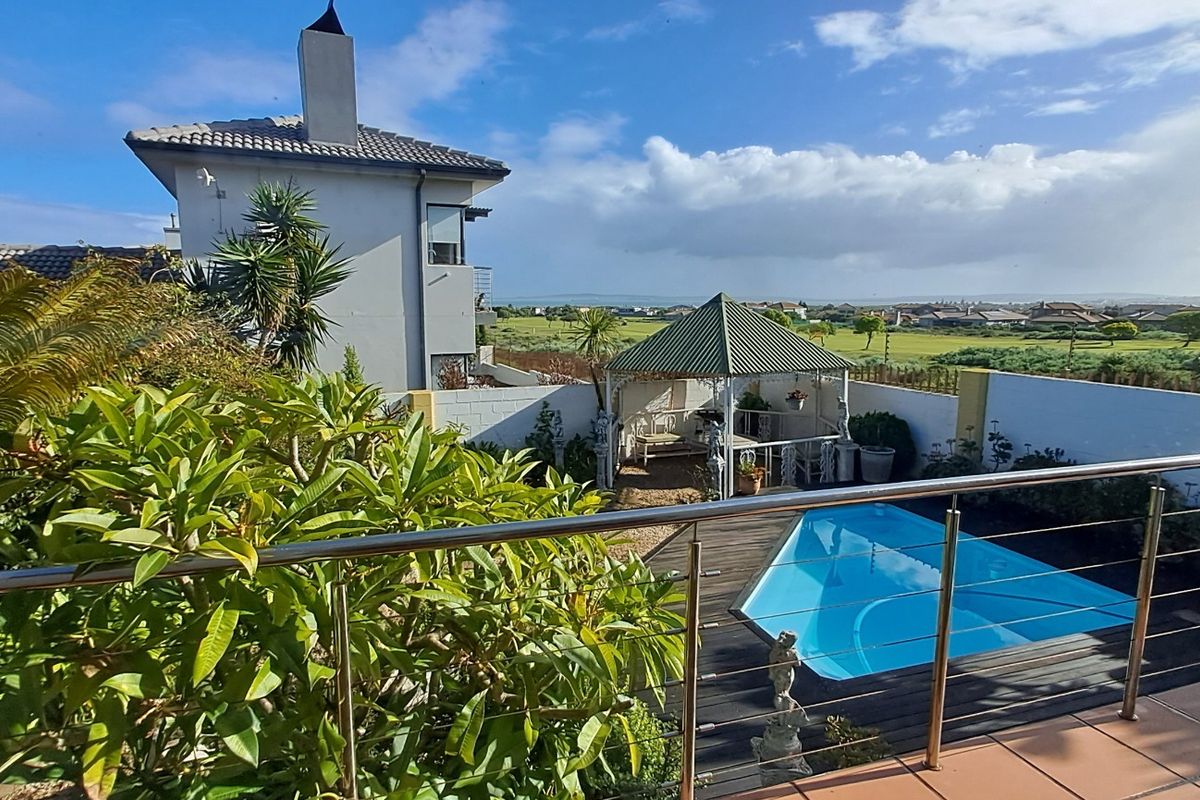Rear exterior view featuring a swimming pool, tiled patio with stainless steel balustrade, and a garden gazebo overlooking the surrounding landscape.