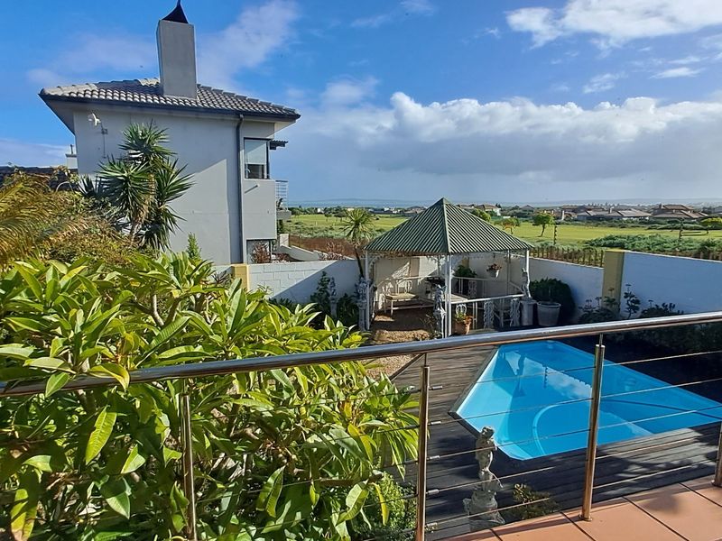Rear exterior view featuring a swimming pool, tiled patio with stainless steel balustrade, and a garden gazebo overlooking the surrounding landscape.