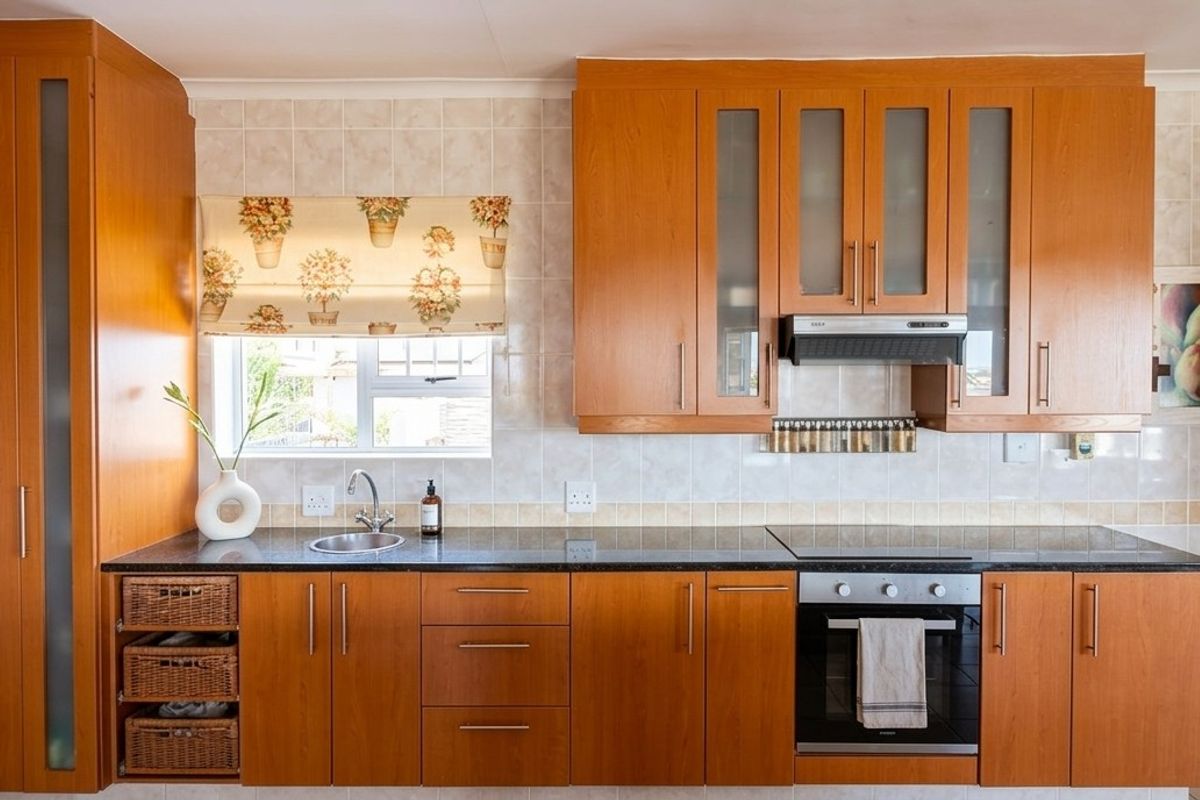 A functional kitchen featuring warm-toned wood cabinetry, dark laminate countertops, a built-in oven, and a tiled backsplash with a window for natural light.