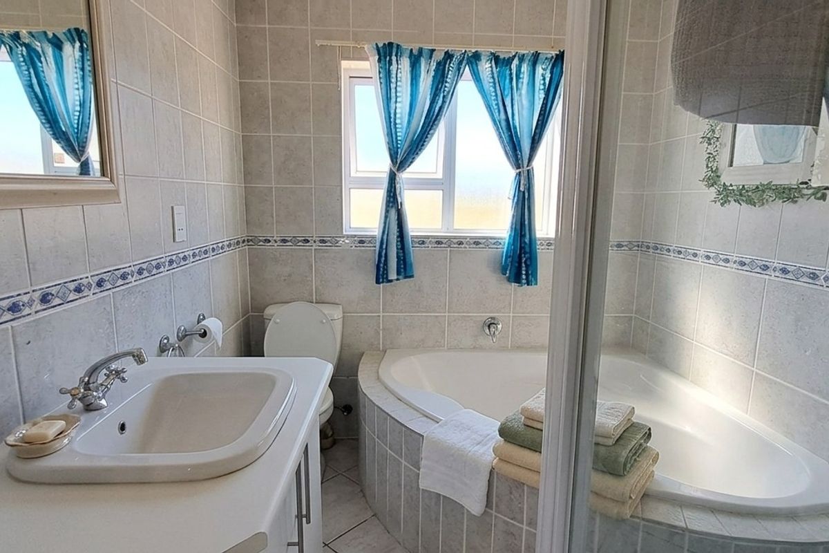 A functional bathroom featuring a corner bathtub, built-in vanity with basin, toilet, and tiled finishes throughout.