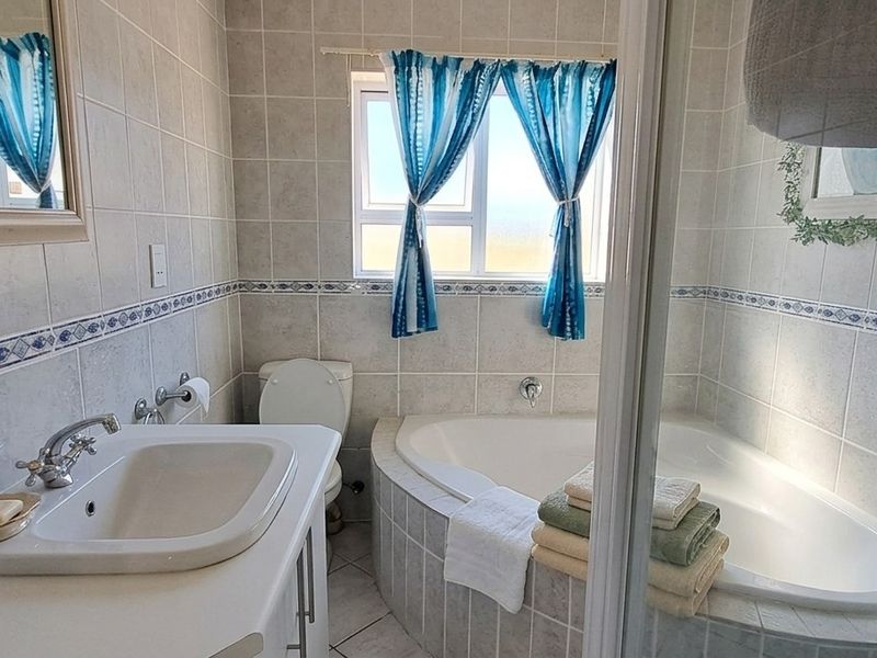 A functional bathroom featuring a corner bathtub, built-in vanity with basin, toilet, and tiled finishes throughout.