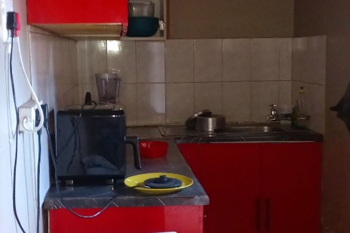 A compact kitchen featuring red cabinetry, a stainless steel sink, tiled backsplash, and tiled flooring.