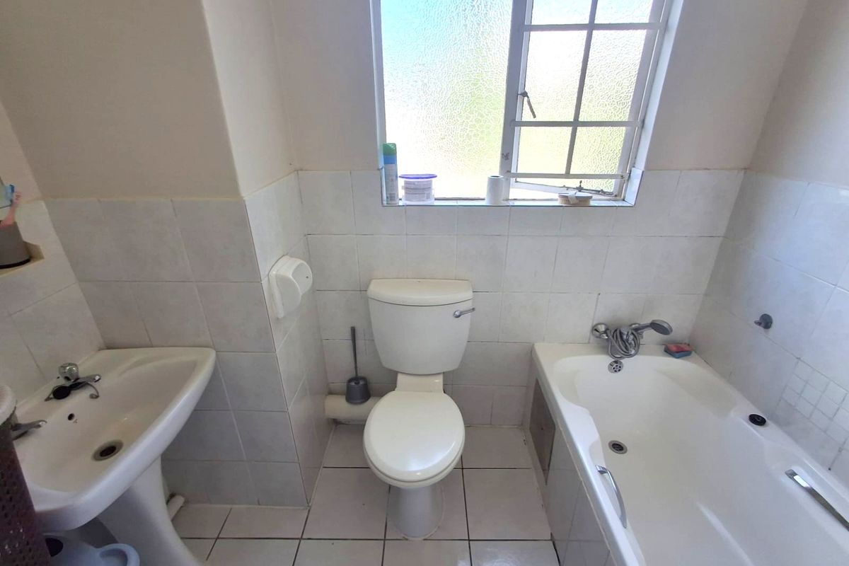 A functional bathroom featuring a pedestal basin, a standard toilet, and a bathtub with a shower mixer, finished with white wall and floor tiles.