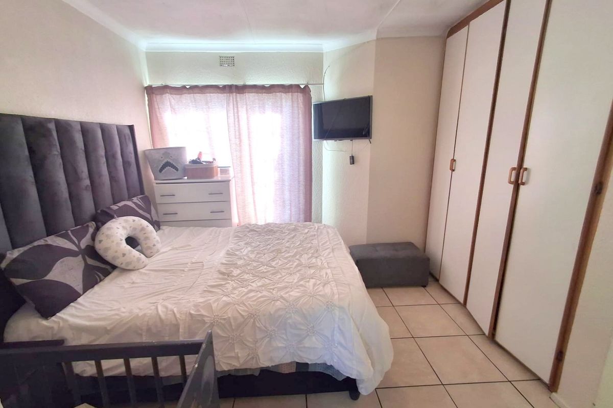 A bedroom featuring built-in wardrobes, tiled flooring, and a window with curtains.