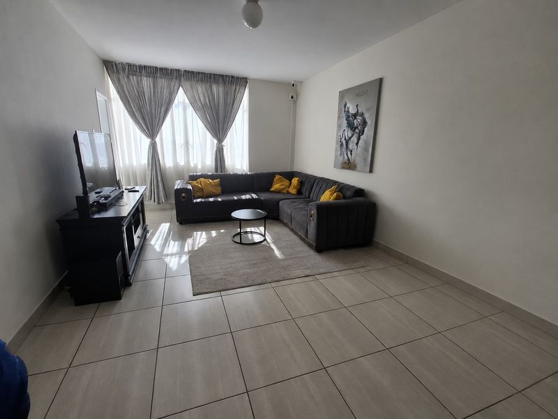 A well-lit living room featuring neutral tiled flooring and large windows with curtains, providing a comfortable and functional space.