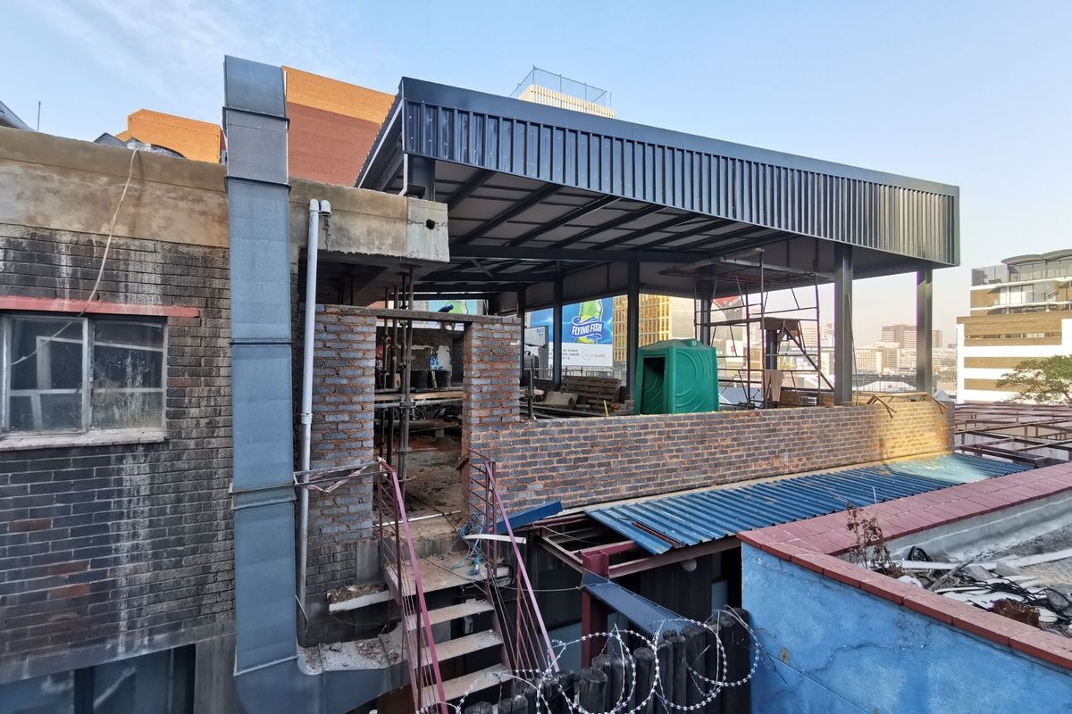 An exterior view of a commercial property currently undergoing construction, featuring exposed brickwork, a steel roof structure, and metal extraction ducting.