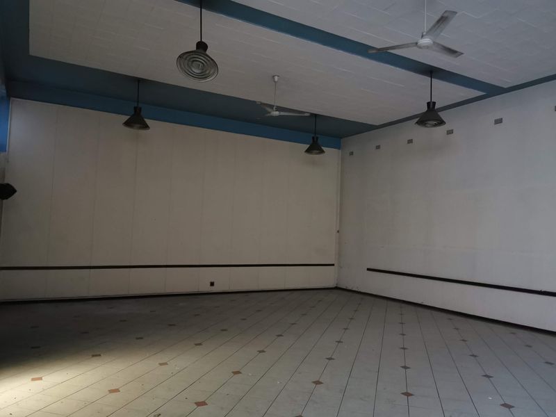 A spacious, empty commercial open-plan area featuring tiled flooring, ceiling fans, and industrial-style pendant lighting, suitable for various business configurations.